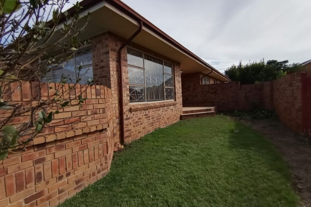 Rear view of a face brick house featuring a small lawn, brick boundary walls, and security-barred windows.