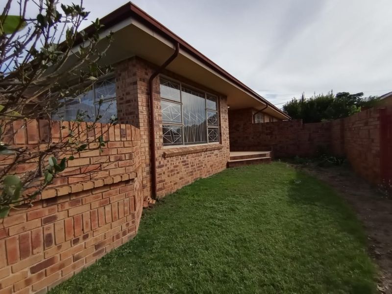 Rear view of a face brick house featuring a small lawn, brick boundary walls, and security-barred windows.