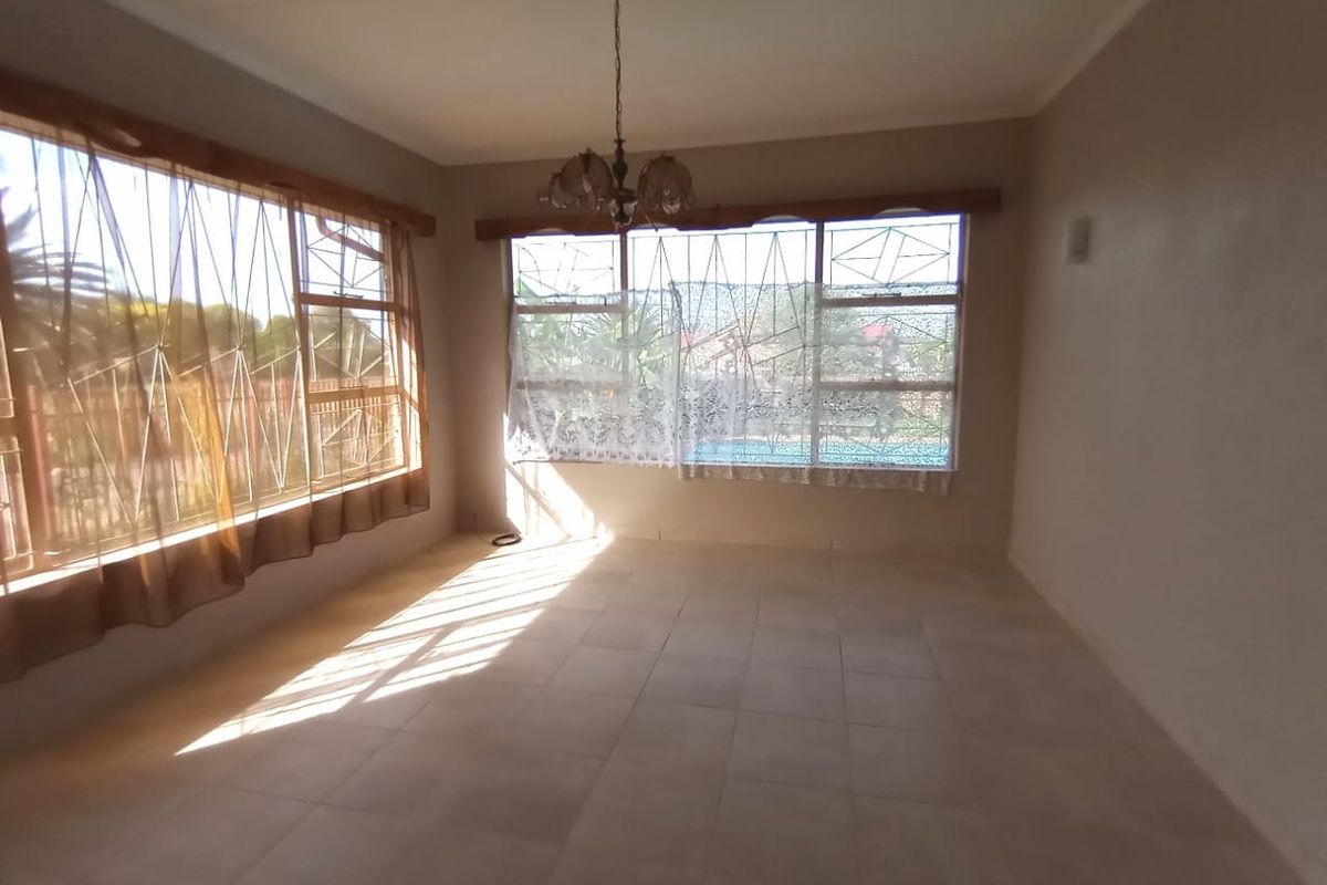 A bright, empty living room featuring tiled flooring, large windows with security bars, and a central ceiling light fixture.