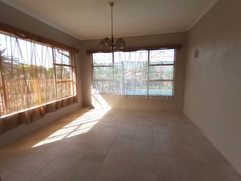 A bright, empty living room featuring tiled flooring, large windows with security bars, and a central ceiling light fixture.