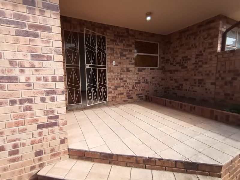 A covered patio area featuring face brick walls, tiled flooring, and a built-in brick planter box, providing a functional outdoor space.