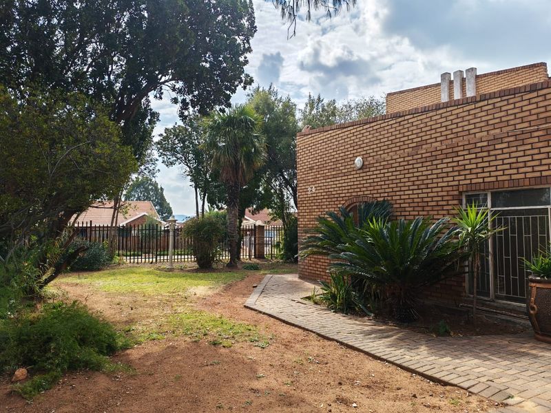 A rear exterior view of a face brick house featuring a paved walkway, established garden, and secure metal perimeter fencing.