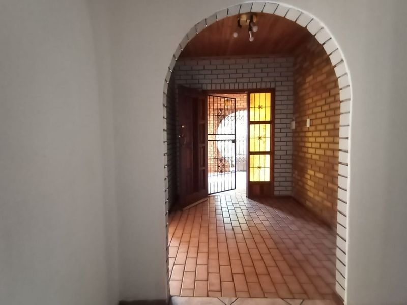An inviting entrance hall featuring a distinctive arched doorway, exposed brickwork, tiled flooring, and a secure timber door with decorative glass panels.