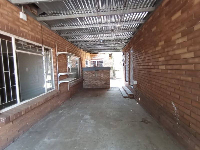 A covered outdoor patio area featuring exposed brick walls, a corrugated metal roof, and a built-in brick counter, offering potential for an entertainment space.