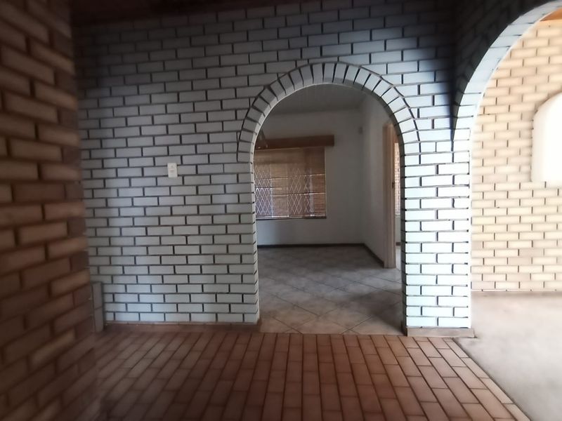 An empty living area featuring distinctive arched brick doorways, exposed brickwork, and tiled flooring, offering a blank canvas for interior design.