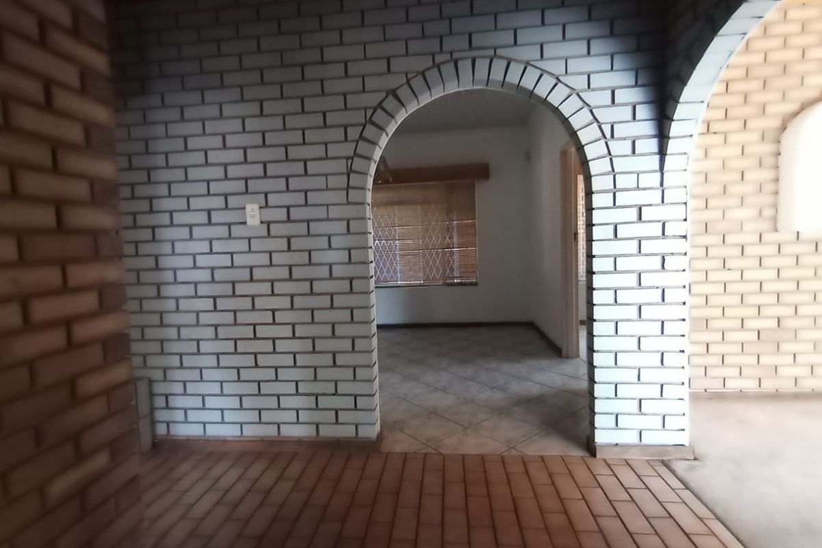 An empty living area featuring distinctive arched brick doorways, exposed brickwork, and tiled flooring, offering a blank canvas for interior design.