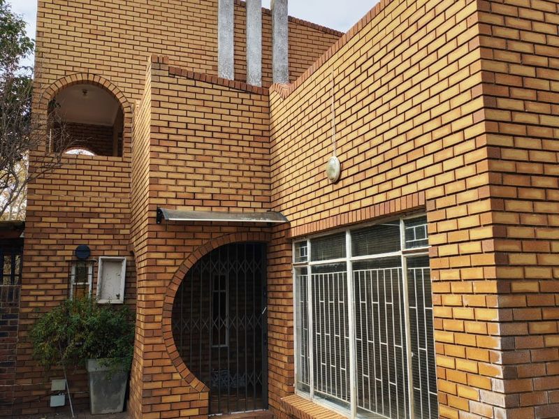 Front elevation of a face brick house featuring an arched entrance, security gates, and a paved walkway leading to the main door.