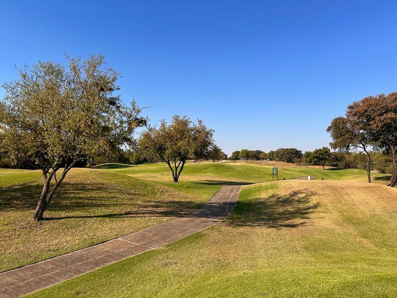 A scenic view of a well-maintained residential landscape featuring rolling green lawns, mature trees, and a paved walkway.