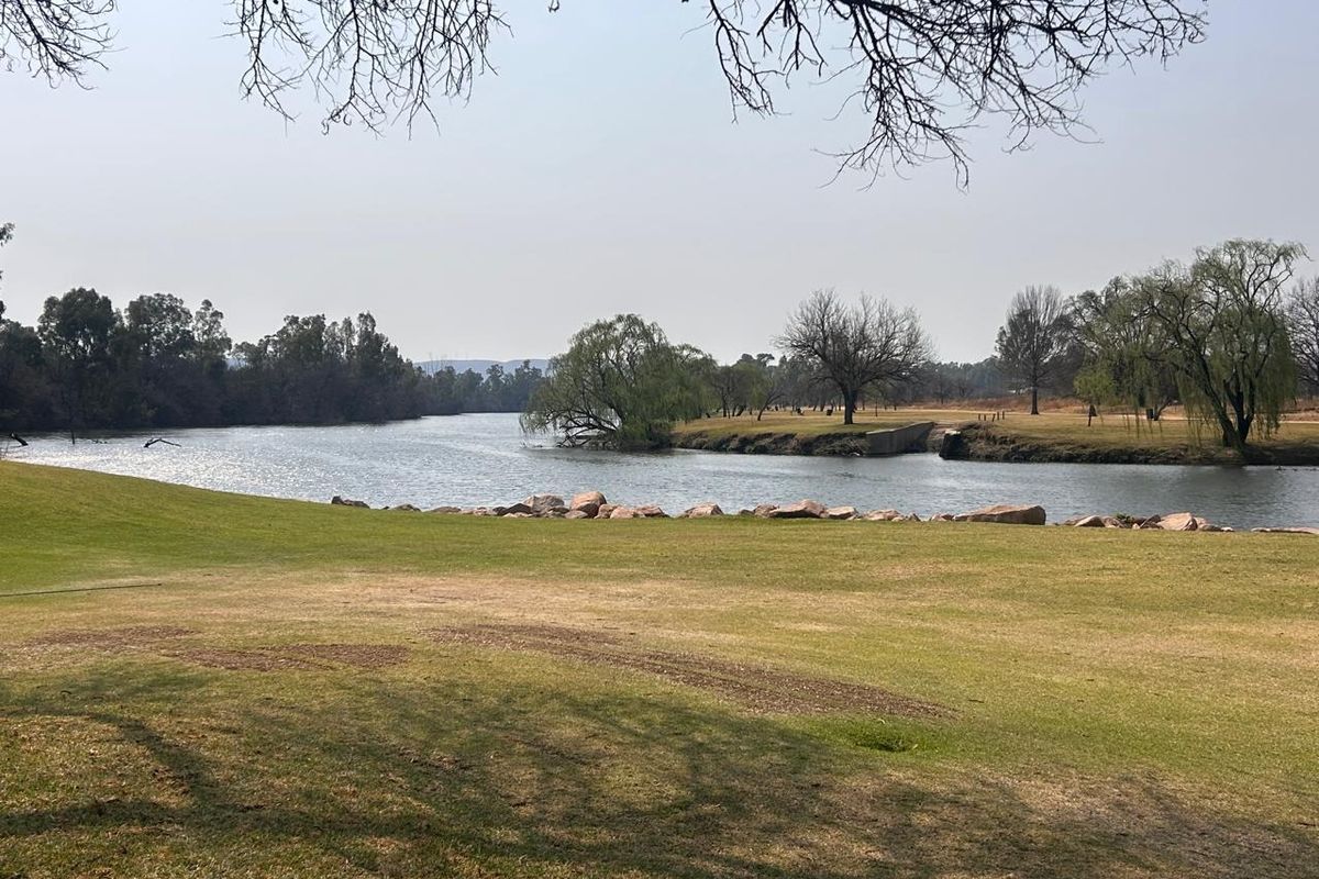 A scenic view of the riverfront featuring a well-maintained lawn and mature trees along the water's edge.
