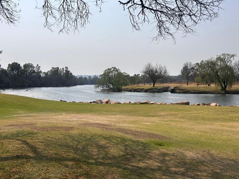 A scenic view of the riverfront featuring a well-maintained lawn and mature trees along the water's edge.