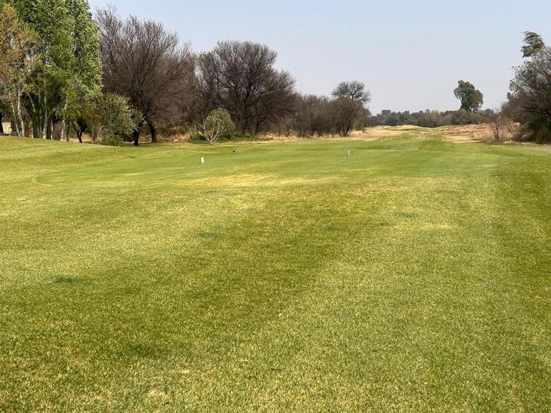 A view of a well-maintained open grass area with mature trees, characteristic of a residential estate or golf course setting.