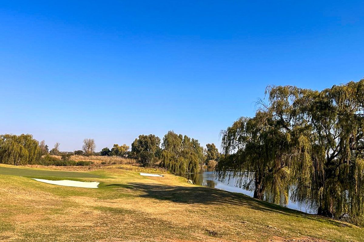 A scenic view of a golf course fairway adjacent to a tranquil lake, featuring mature weeping willow trees and natural landscaping.