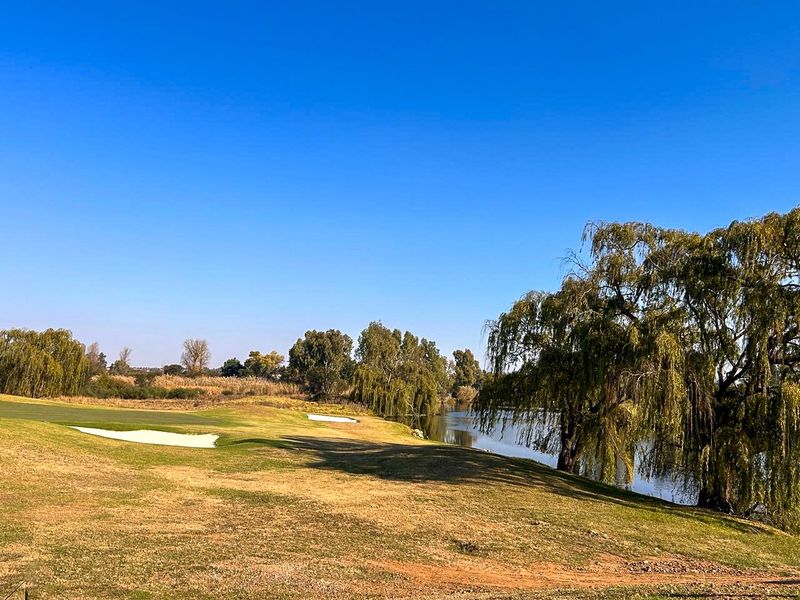 A scenic view of a golf course fairway adjacent to a tranquil lake, featuring mature weeping willow trees and natural landscaping.