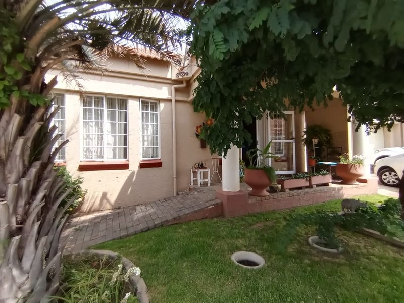 Front facade of the townhouse featuring a paved access ramp, tiled roof, and established garden area with a covered entrance porch.