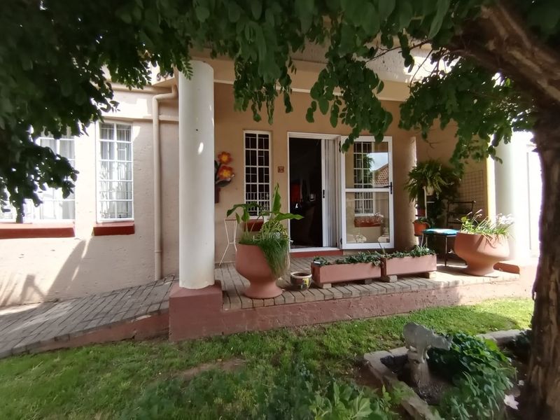 Front entrance of the townhouse featuring a covered porch, concrete columns, and a paved access ramp with security gates and bars.