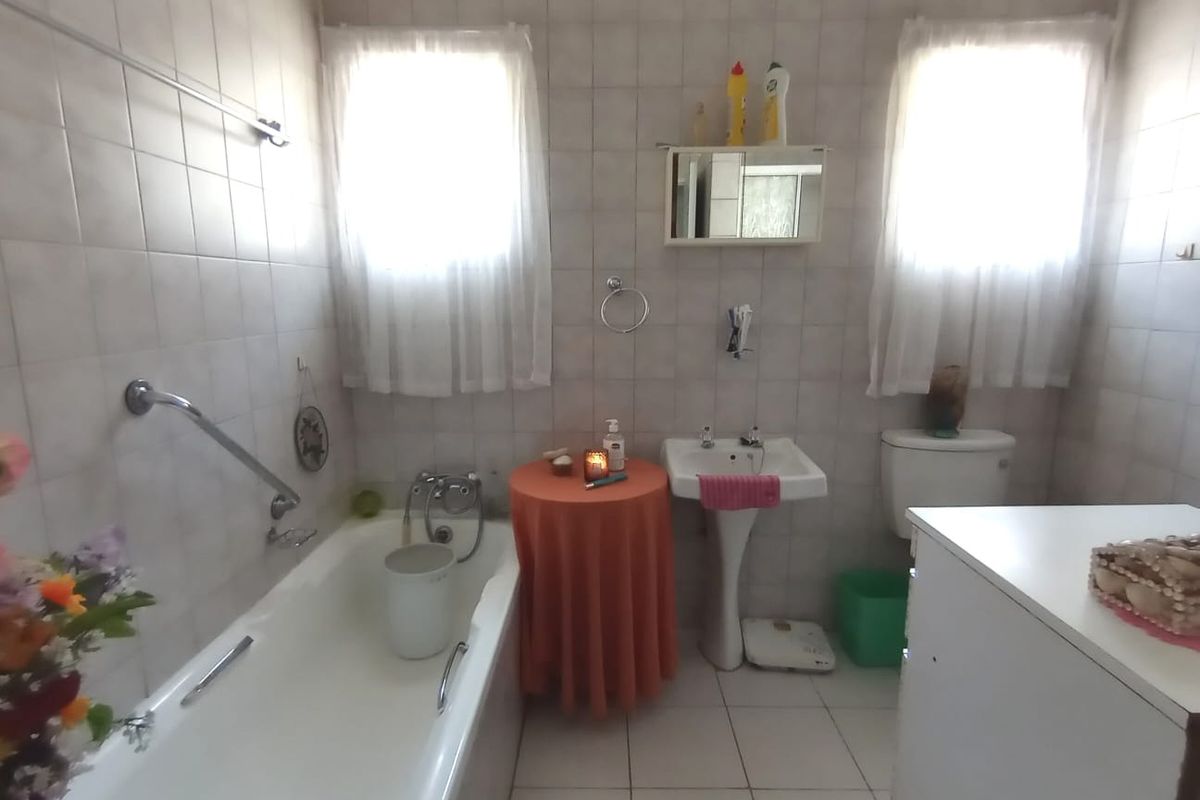 A functional bathroom featuring a bathtub with a grab rail, a pedestal basin, and a toilet, finished with neutral wall and floor tiling.
