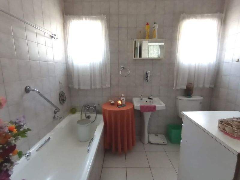 A functional bathroom featuring a bathtub with a grab rail, a pedestal basin, and a toilet, finished with neutral wall and floor tiling.