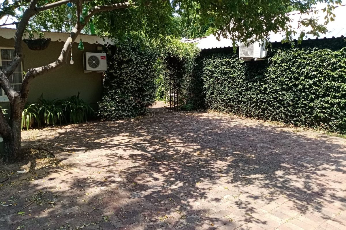 A private rear courtyard featuring brick paving, established greenery, and wall-mounted air conditioning units, providing a shaded outdoor space.