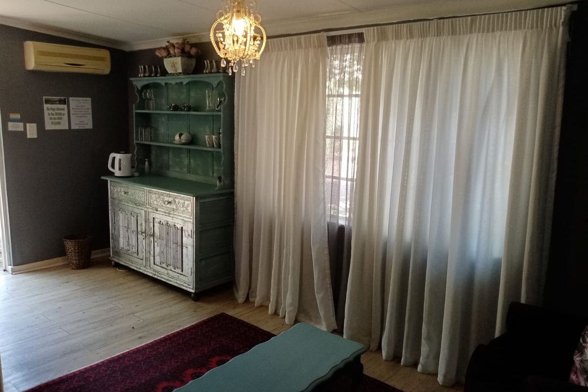 A living room featuring laminate flooring, a wall-mounted air conditioning unit, and large windows dressed with floor-to-ceiling curtains.