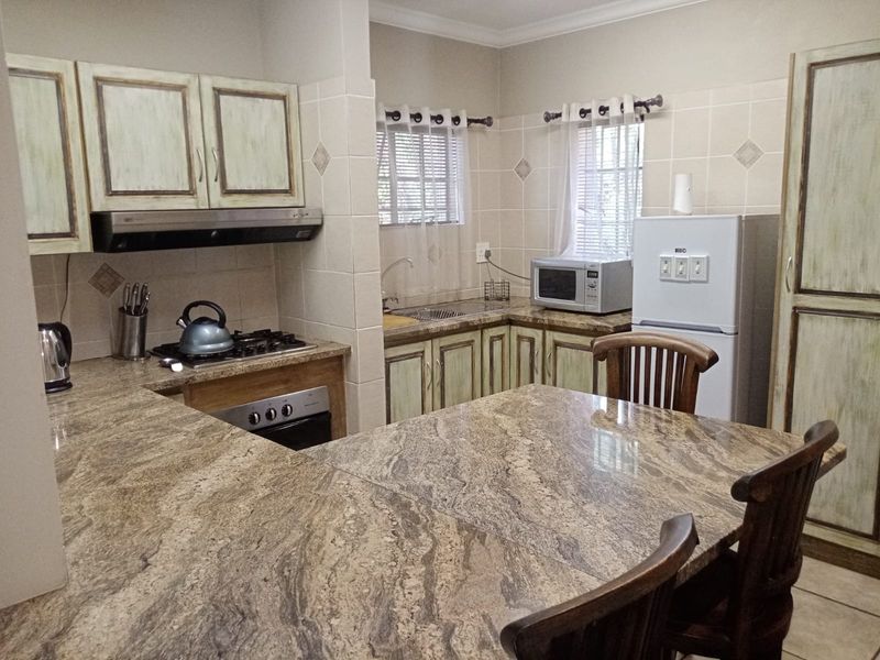A functional kitchen featuring granite countertops, built-in cabinetry, a gas hob with extractor fan, and a tiled backsplash.