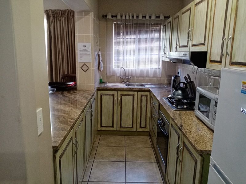 A functional kitchen featuring granite countertops, built-in cabinetry, a gas hob with extractor fan, and tiled flooring.