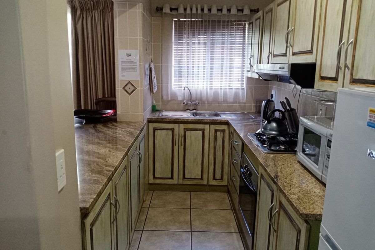 A functional kitchen featuring granite countertops, built-in cabinetry, a gas hob with extractor fan, and tiled flooring.