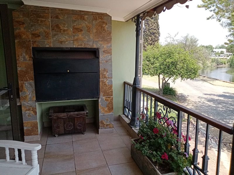 Covered balcony featuring a built-in braai, stone cladding, and wrought iron railings, offering scenic views of the surrounding landscape and water.