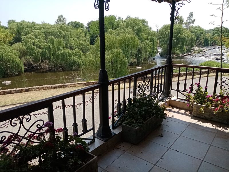 A covered balcony featuring tiled flooring and decorative wrought iron railings, offering scenic views of the river and surrounding greenery.