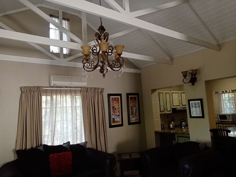 Open plan living area featuring a high vaulted ceiling with exposed trusses, integrated kitchen cabinetry, and a split-system air conditioner.