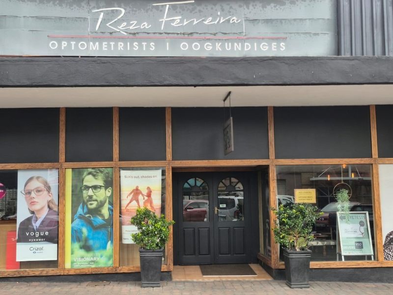 Front facade of a commercial optometrist practice featuring timber-framed display windows and a double-door entrance.
