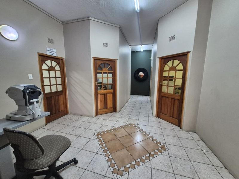 A commercial hallway featuring tiled flooring and multiple wooden panelled doors leading to individual office or consultation rooms.