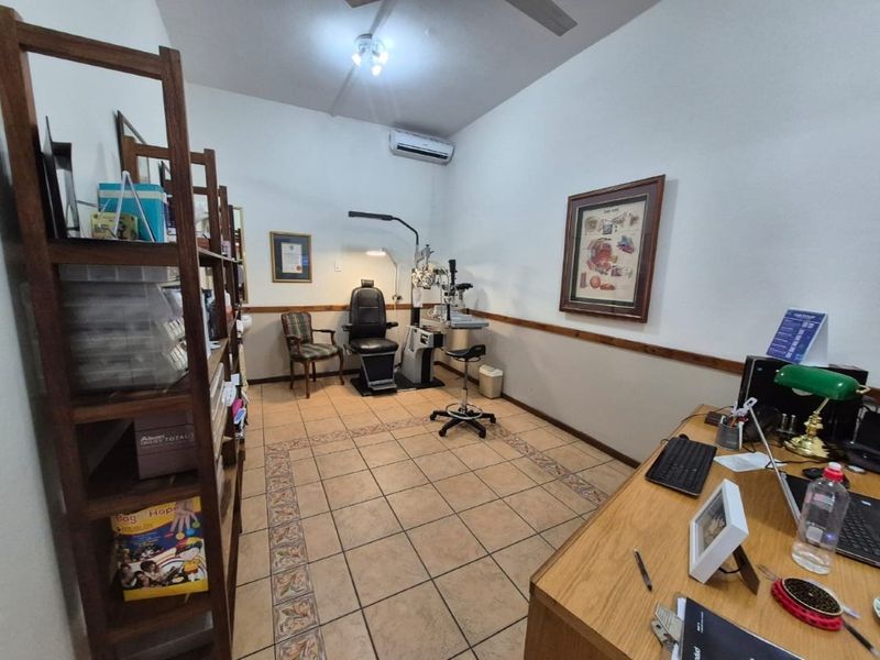 A functional commercial office or examination room featuring ceramic tile flooring, chair rail molding, and a wall-mounted split-system air conditioning unit.
