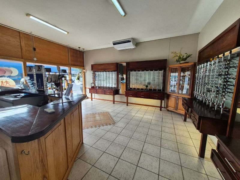 Commercial retail space featuring built-in wooden display cabinetry, tiled flooring, and large storefront windows, suitable for an optical or boutique retail business.