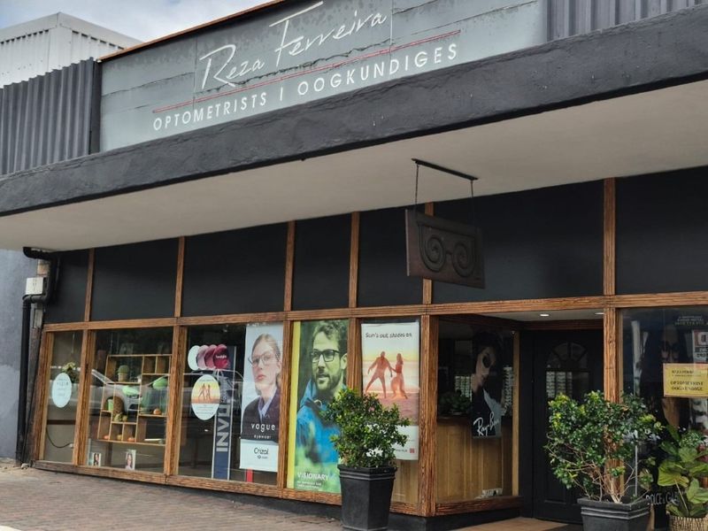 Front facade of a commercial optometrist practice featuring large display windows, wooden framing, and prominent business signage.
