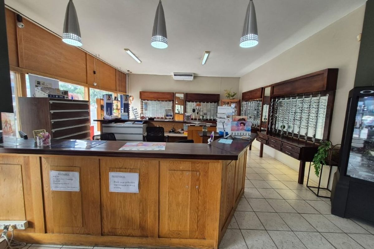 Commercial office space featuring a large built-in wooden reception counter, wall-mounted display shelving, tiled flooring, and integrated ceiling lighting.