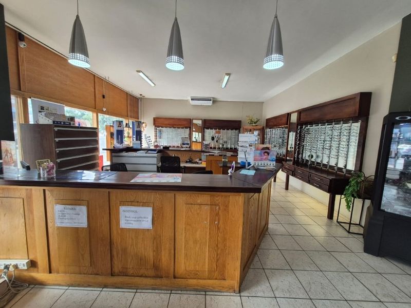 Commercial office space featuring a large built-in wooden reception counter, wall-mounted display shelving, tiled flooring, and integrated ceiling lighting.