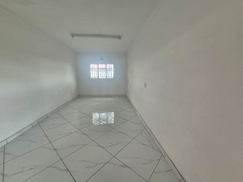 An empty, versatile industrial space featuring white walls, tiled flooring, and a security-fitted window.