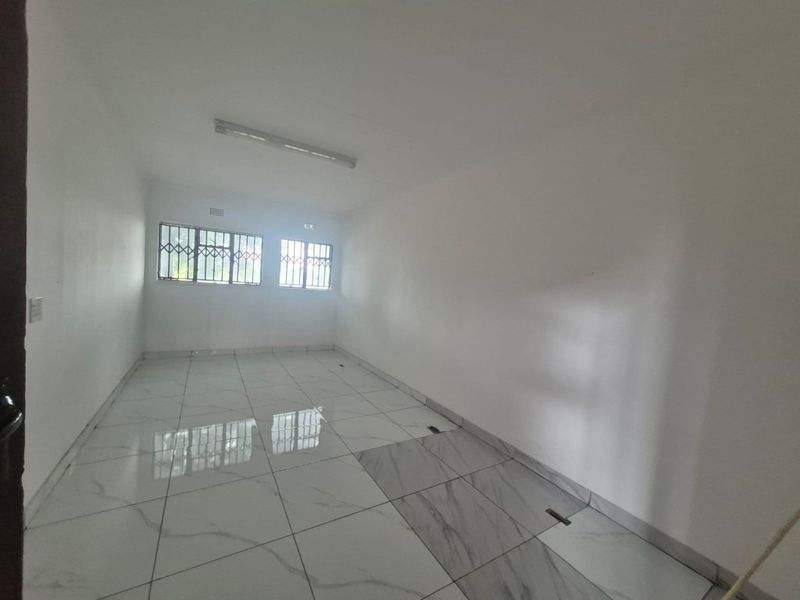 An empty, open-plan office space featuring white walls, tiled flooring, and windows fitted with security bars.