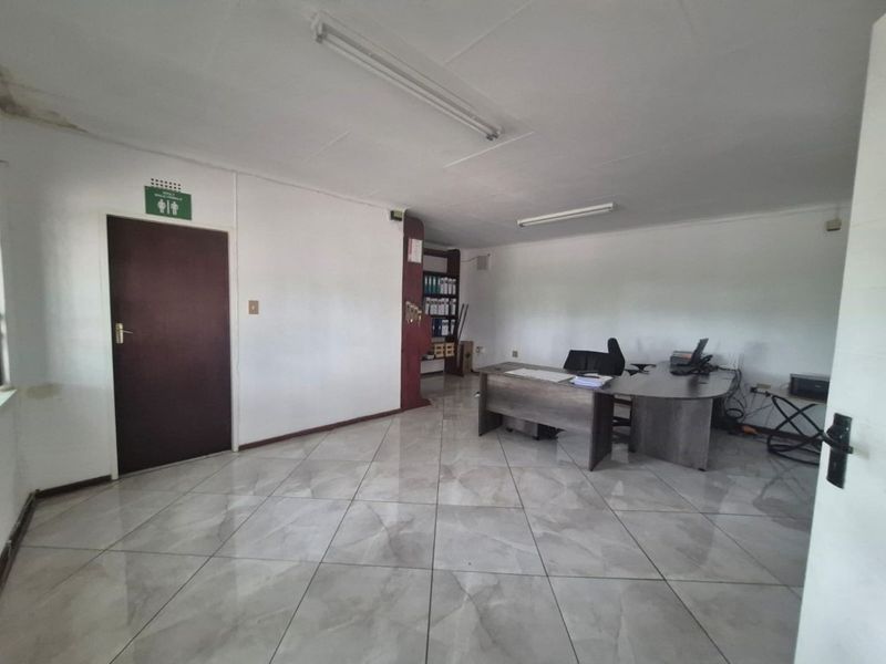 A functional office space featuring tiled flooring, built-in shelving, and fluorescent lighting, with visible signs of ceiling water damage.