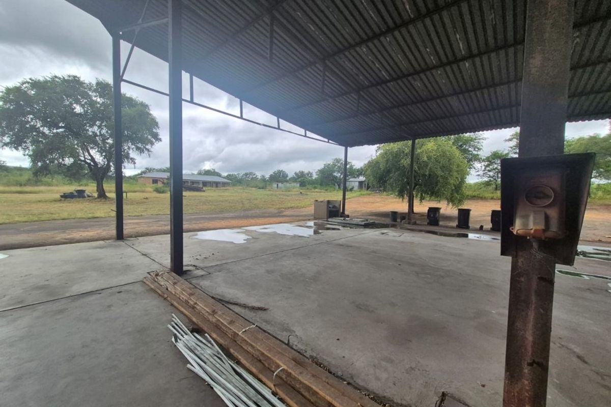 An open-sided industrial utility space featuring a corrugated metal roof, steel support structure, and concrete flooring, suitable for storage or workshop use.