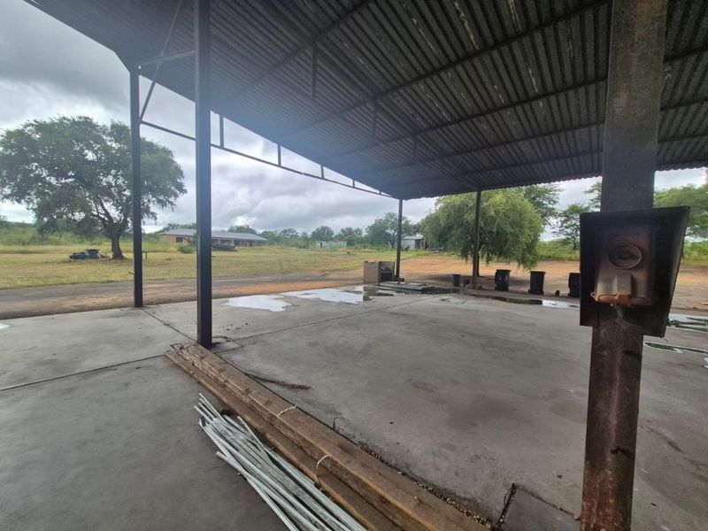 An open-sided industrial utility space featuring a corrugated metal roof, steel support structure, and concrete flooring, suitable for storage or workshop use.
