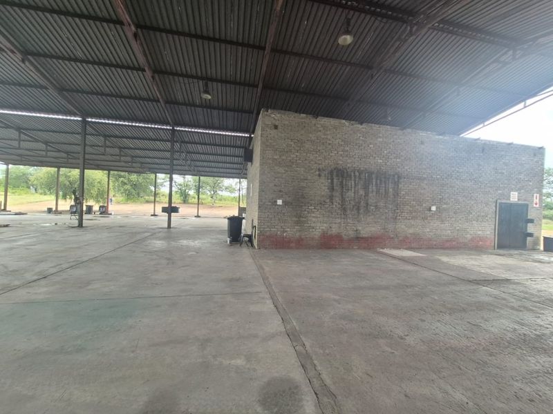 Large industrial utility space featuring a high corrugated metal roof, concrete flooring, and exposed brickwork, suitable for storage or workshop operations.