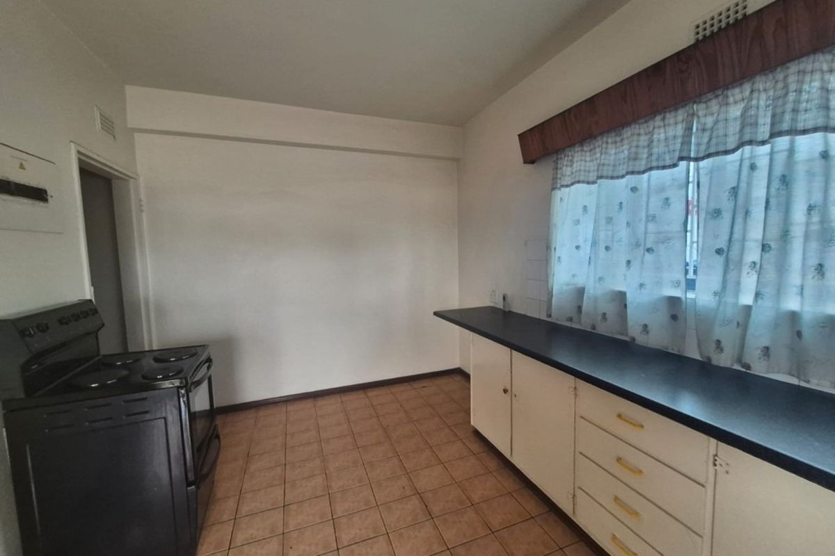 A functional kitchen space featuring tiled flooring, built-in cabinetry with laminate countertops, and a freestanding stove, offering potential for modern renovation.