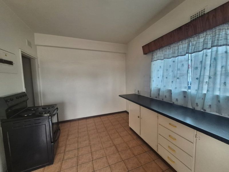 A functional kitchen space featuring tiled flooring, built-in cabinetry with laminate countertops, and a freestanding stove, offering potential for modern renovation.