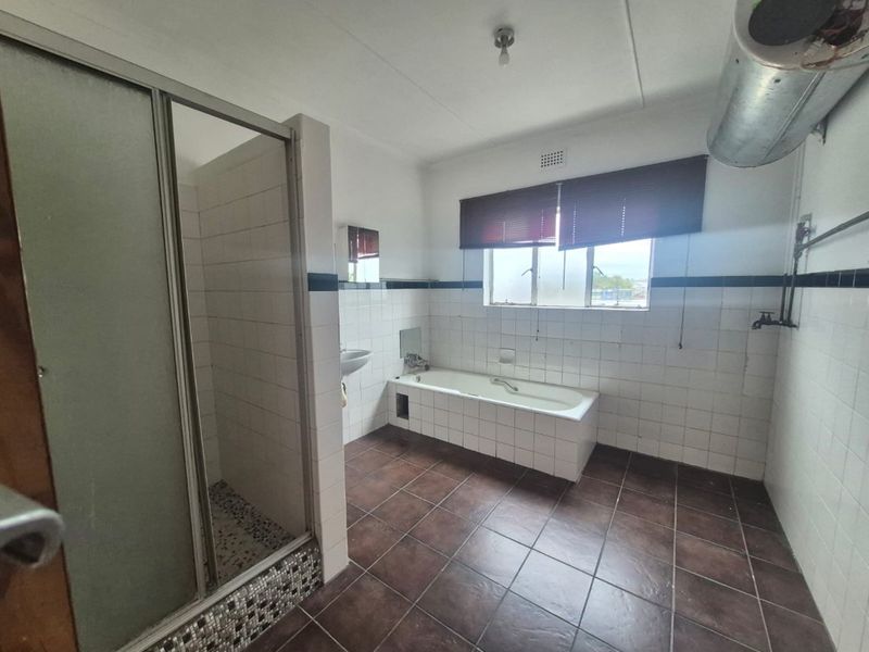A spacious, dated bathroom featuring a separate shower enclosure, bathtub, and washbasin with tiled finishes throughout.