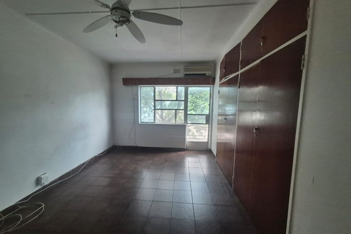 An empty bedroom featuring tiled flooring, built-in wooden cupboards, a ceiling fan, and an air conditioning unit.