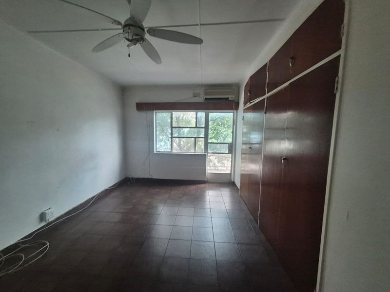An empty bedroom featuring tiled flooring, built-in wooden cupboards, a ceiling fan, and an air conditioning unit.