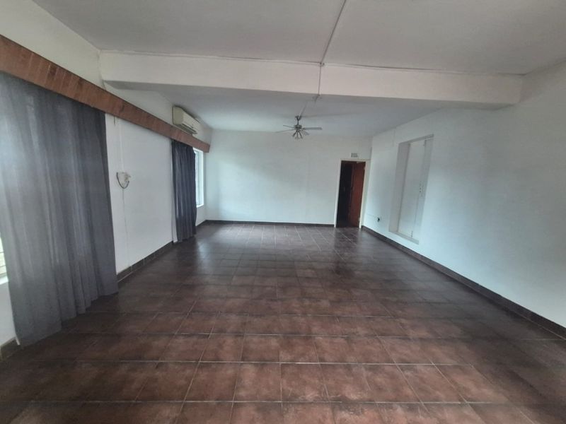 A spacious, empty living area featuring tiled flooring, a ceiling fan, and a wall-mounted air conditioning unit.