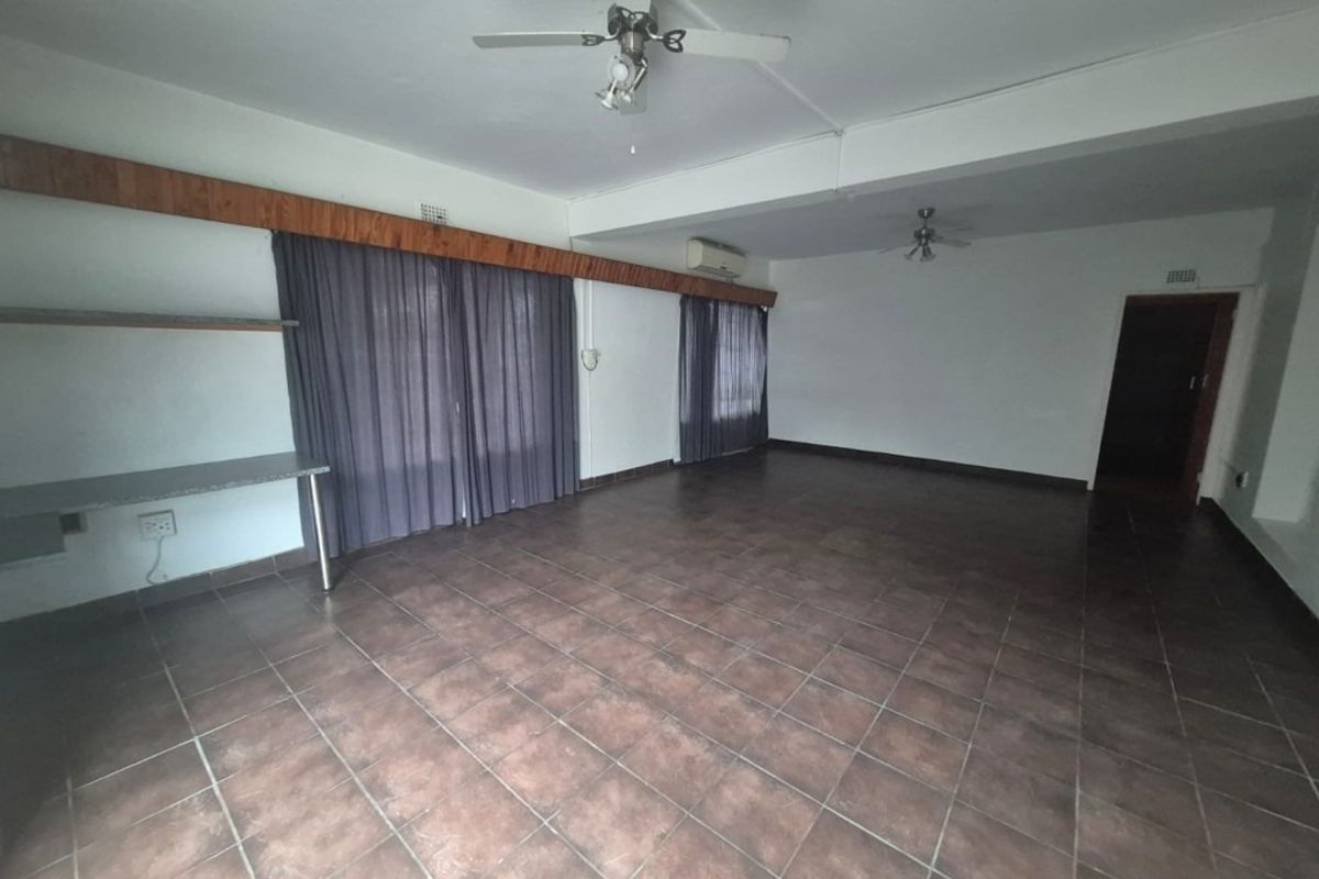 Spacious, empty living area featuring tiled flooring, ceiling fans, air conditioning, and built-in shelving with access to outdoor space via sliding doors.