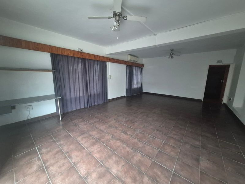 Spacious, empty living area featuring tiled flooring, ceiling fans, air conditioning, and built-in shelving with access to outdoor space via sliding doors.
